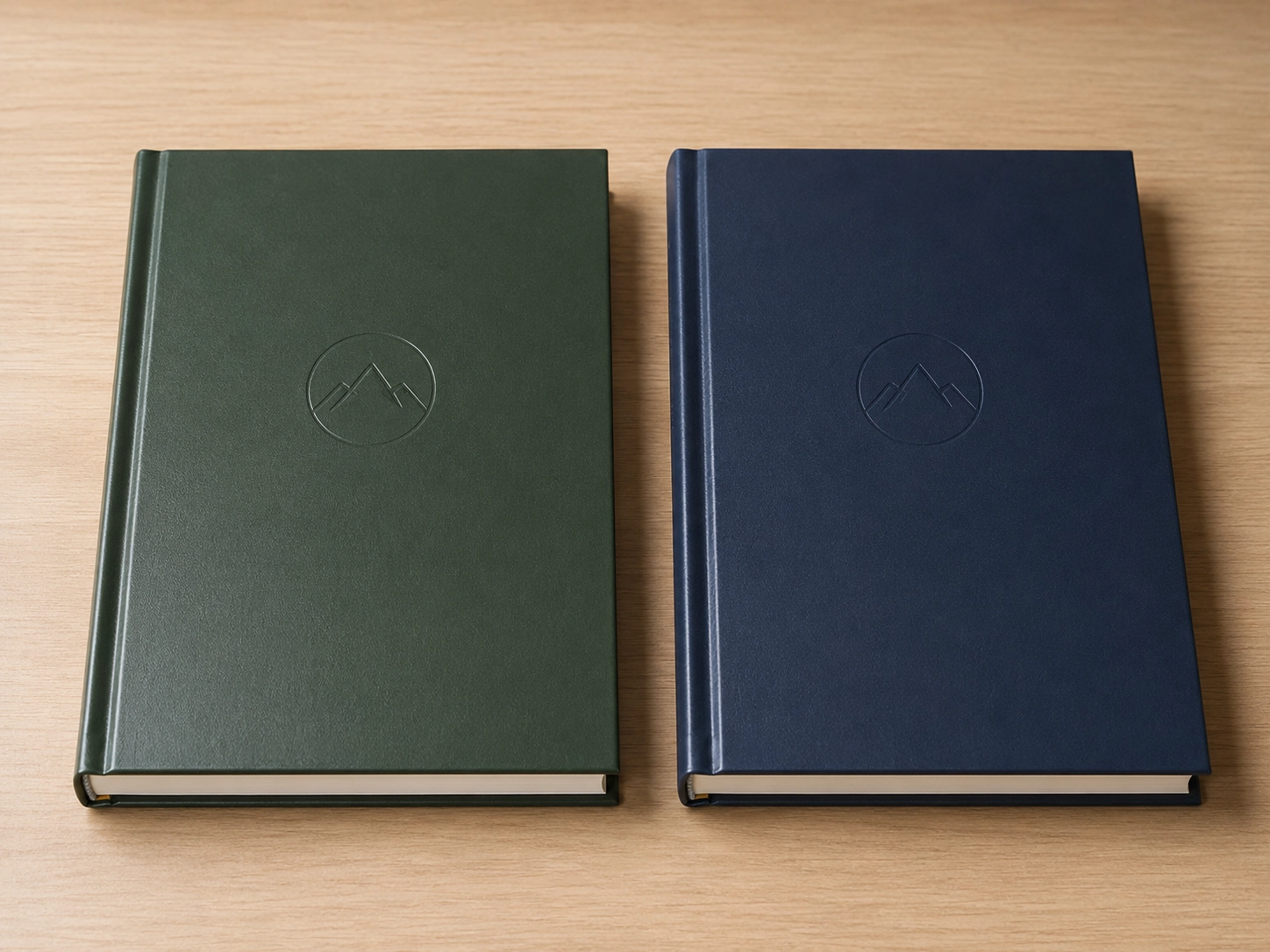 Two custom hardbound sketchbooks side by side on a desk showing cover lamination debossed logo and casebinding details